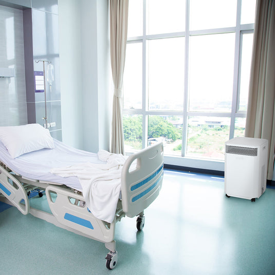 A hospital ward with single unoccupied bed. An INOVA air purifier is sitting near a window, quietly cleaning the air, removing harmful viruses, keeping the staff and patients safe from the risk of infection.